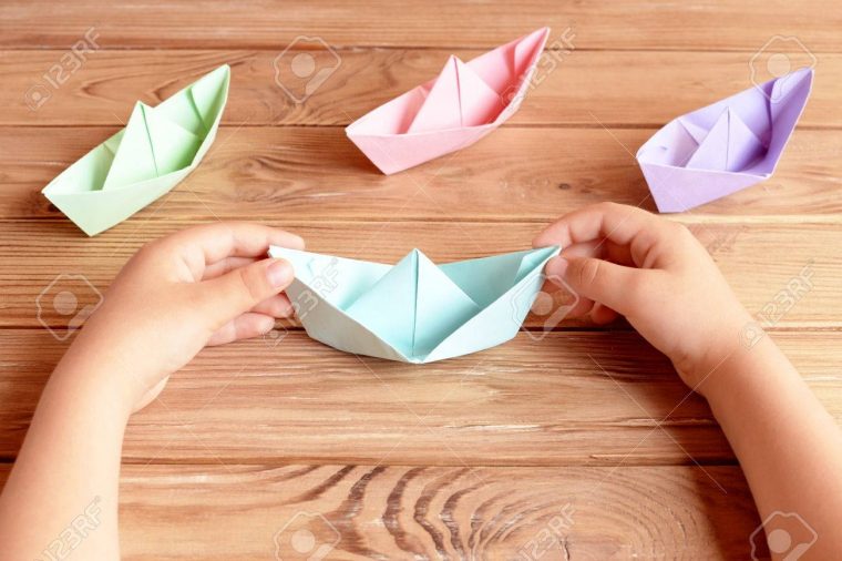 Enfant Détient Le Navire De L'origami Dans Ses Mains. Navires Colorés  Papier Origami Pliage Sur Une Table En Bois. Préscolaire Et Papier De  Maternelle à Pliage Papier Enfant