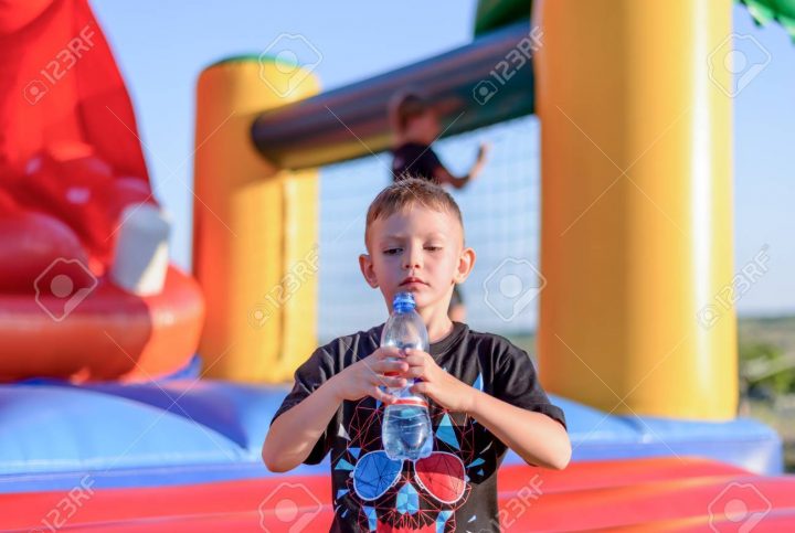 Jeune Garçon Consommation D'eau Embouteillée Comme Il Se Tient Devant Un  Château Coloré De Saut En Plastique À Un Terrain De Jeux Ou Champ De Foire dedans Jeux De Saut Dans L Eau