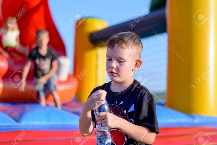 Jeune Garçon Consommation D'eau Embouteillée Comme Il Se Tient Devant Un  Château Coloré De Saut En Plastique À Un Terrain De Jeux Ou Champ De Foire dedans Jeux De Saut Dans L Eau