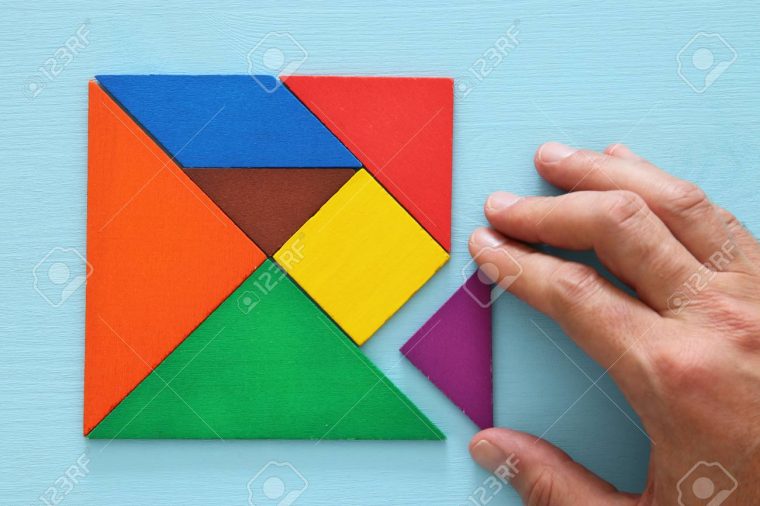 Main De L'homme Tenant Une Pièce Manquante Dans Un Puzzle De Tangram Carré,  Sur Une Table En Bois. destiné Tangram Carré